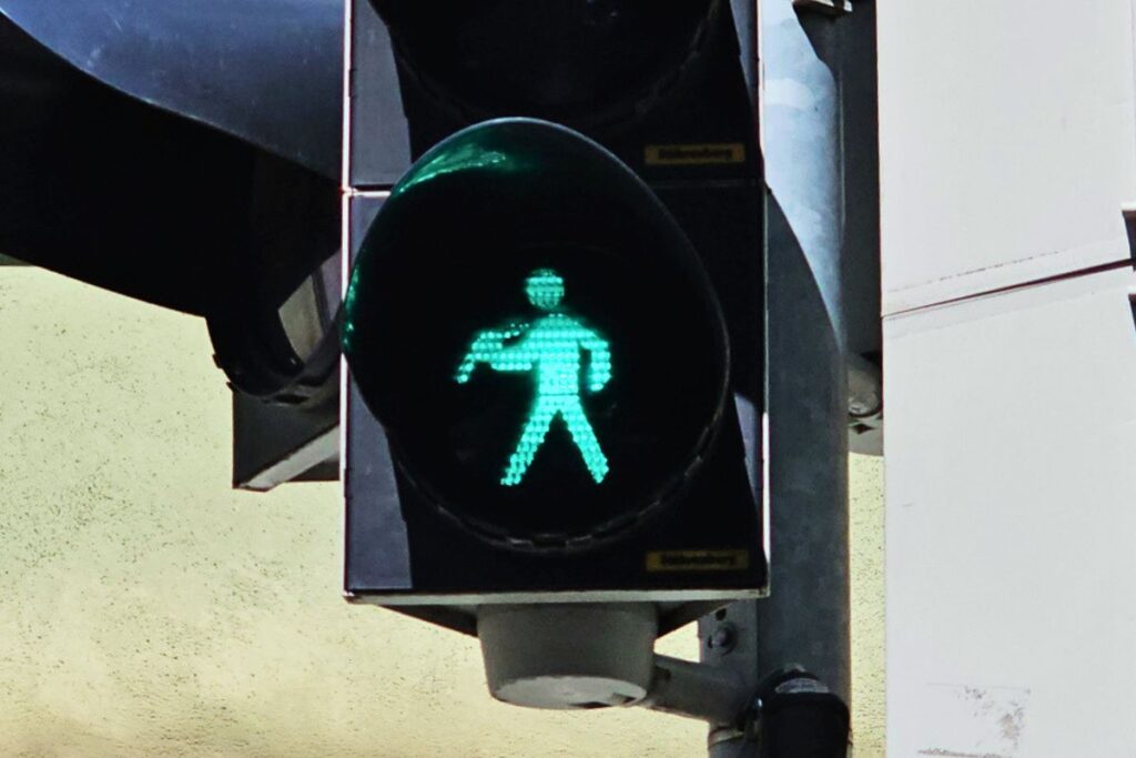 Nahaufnahme einer grünen Fußgängerampel in Coburg, auf der das grüne Ampelmännchen eine Bratwurst in einer Semmel trägt.