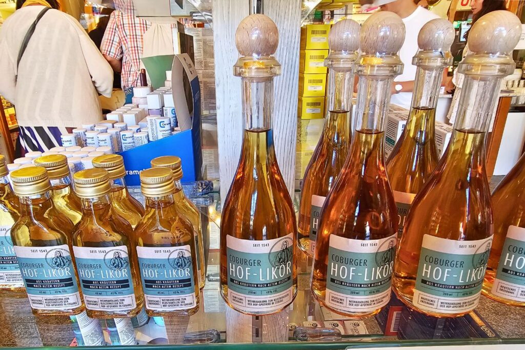 Mehrere Flaschen des traditionellen Coburger Hof-Likörs mit runden Holzverschlüssen und blau-grünen Etiketten in einem Regal der Hof-Apotheke in Coburg.
