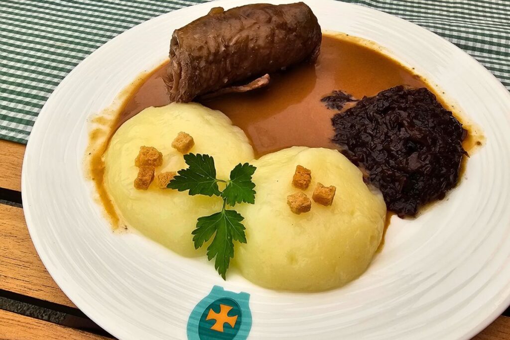 Ein traditionelles fränkisches Gericht mit zwei weichen Coburger Rutschern, einer saftigen Rinderroulade und Rotkohl in dunkler Soße auf einem weißen Teller im Restaurant Goldenes Kreuz in Coburg.