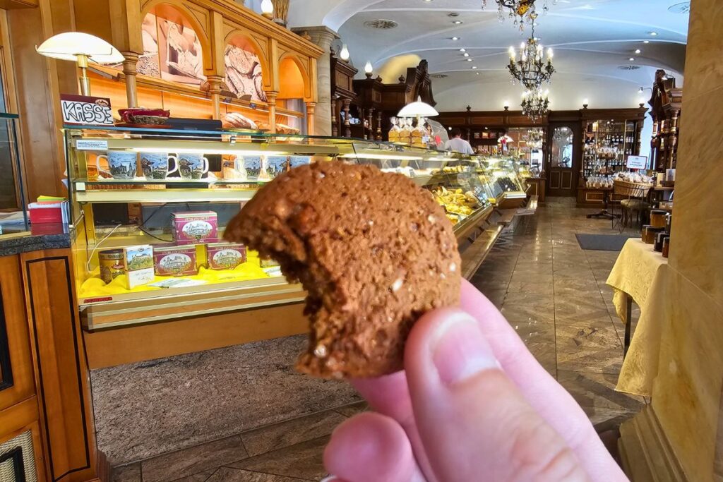 Nahaufnahme einer Hand, die ein rundes, angebissenes Coburger Schmätzchen vor der hölzernen Verkaufstheke der Hofbäckerei Feyler hält.