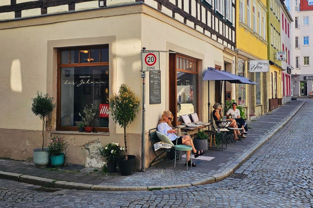 Die Außenansicht des gemütlichen Cafés "das Johann" an einer Straßenecke in der Coburger Altstadt mit historischem Fachwerk und Gästen auf Stühlen im Freien.