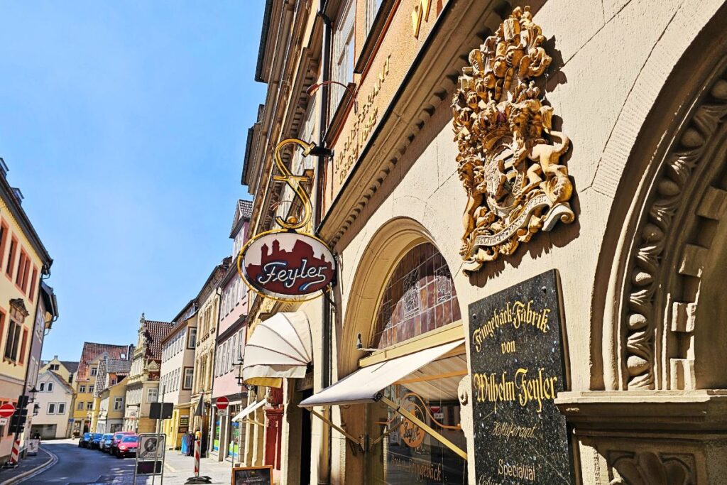 Die historische Fassade der Lebkuchen- und Feinbäckerei Wilhelm Feyler in Coburg mit einem prachtvollen goldenen Hoflieferanten-Wappen und dem runden Ladenschild über dem Eingang.