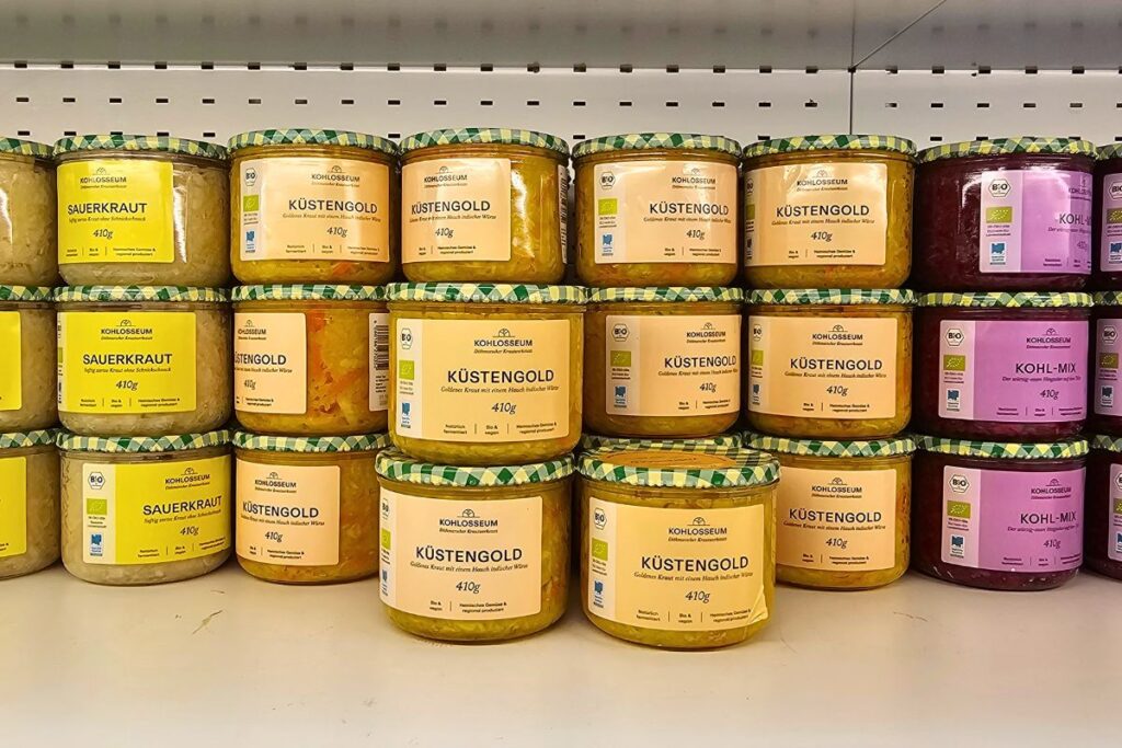 Mehrere Reihen ordentlich aufgereihter Gläser mit Sauerkraut, Küstengold und Kohl-Mix im Verkaufsregal des KOHLosseums.