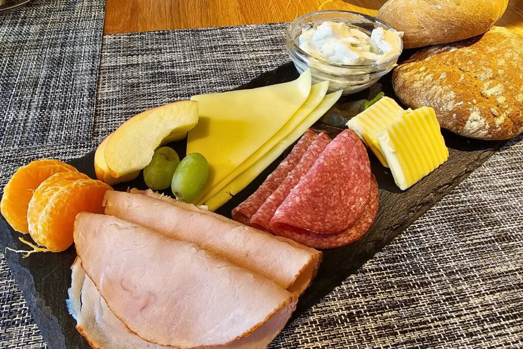 Ein reichhaltiges Frühstück auf einer edlen Schieferplatte mit frischen Brötchen, Käse, Salami, Schinken und Obst in der Neuen Holländerei Meldorf.