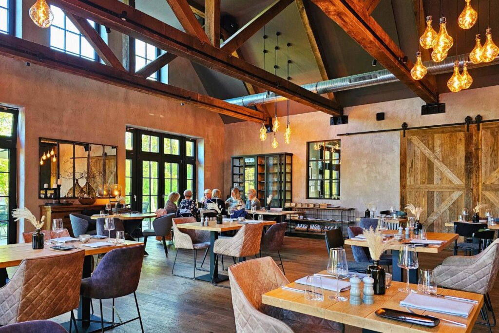 Der großzügige, moderne Innenraum des Restaurants Outer Roads in Brunsbüttel mit hohen, offenen Deckenbalken, warmen Designer-Glühbirnen und besetzten Tischen.