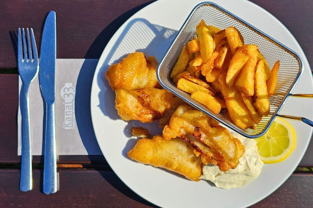 Goldbraun gebackene Fischstücke mit knusprigen Pommes Frites in einem Servierkörbchen und feiner Remoulade auf einem weißen Teller im Restaurant Kanal 33.