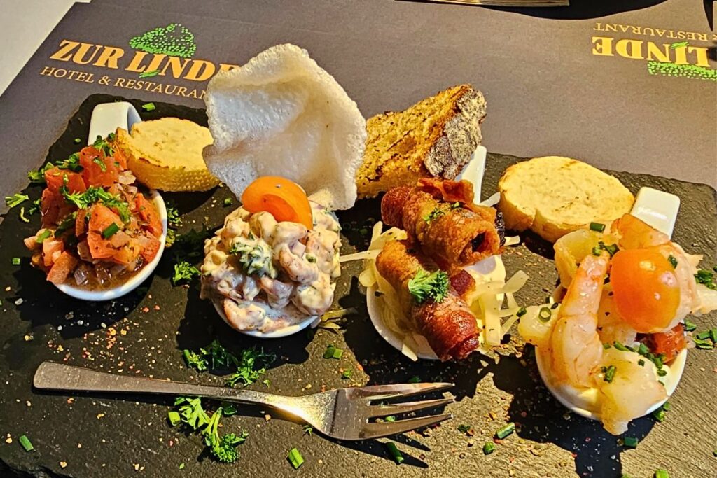Eine rustikale Schieferplatte im Restaurant Zur Linde in Meldorf mit verschiedenen mundgerechten Spezialitäten als Tapas Ditschis Art, darunter feiner Krabbensalat und krosse Speckhäppchen.