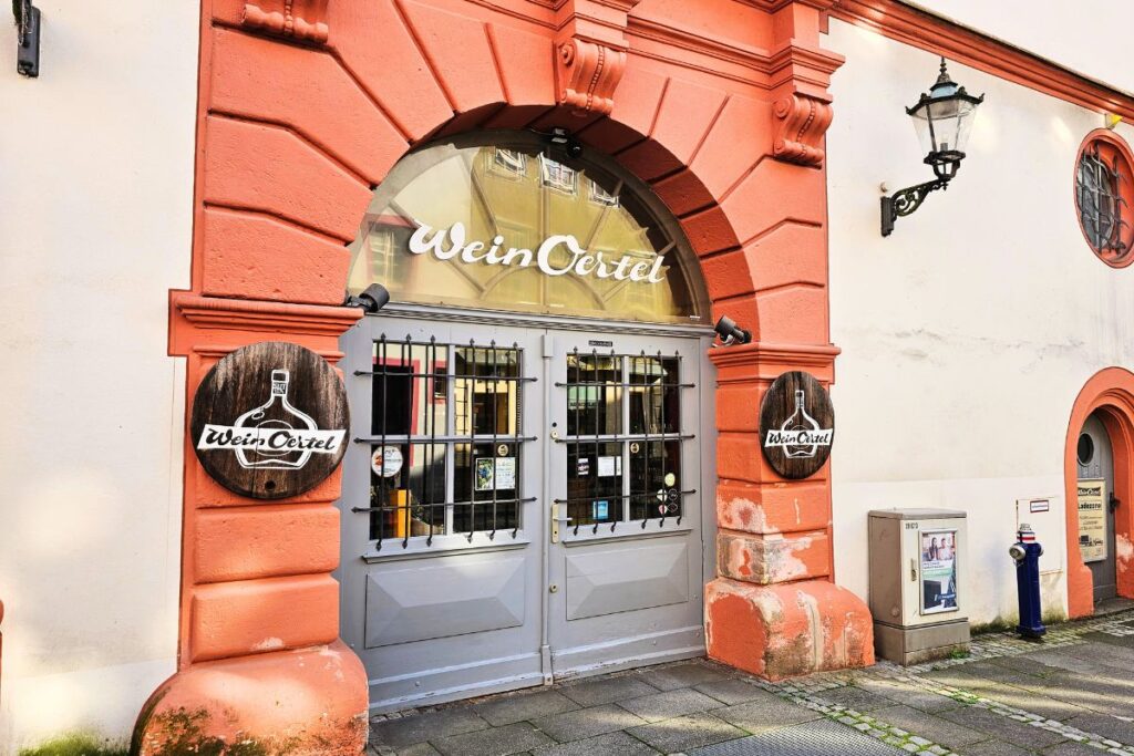 Das historische, rötliche Sandstein-Eingangsportal der traditionsreichen Weinhandlung Wein Oertel in der Altstadt von Coburg mit runden Holzschildern an den Säulen.