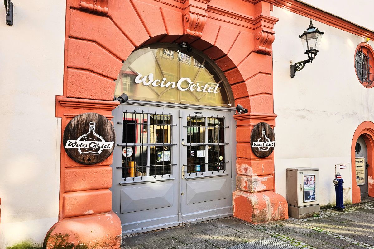 Das historische, rötliche Sandstein-Eingangsportal der traditionsreichen Weinhandlung Wein Oertel in der Altstadt von Coburg mit runden Holzschildern an den Säulen.