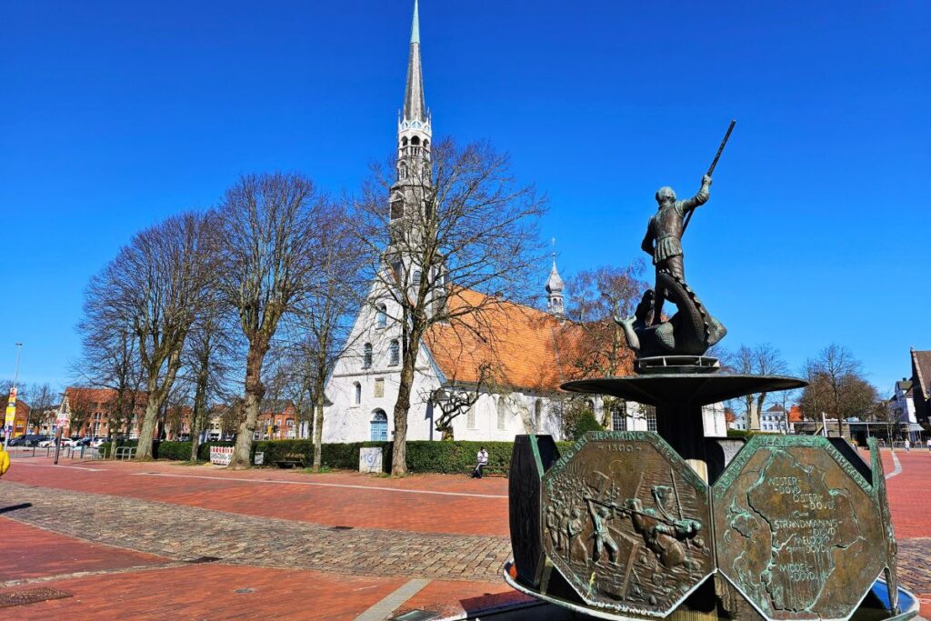 Der St.-Georgs-Brunnen im Vordergrund und die weiße St.-Jürgen-Kirche auf dem Marktplatz in Heide in Dithmarschen.