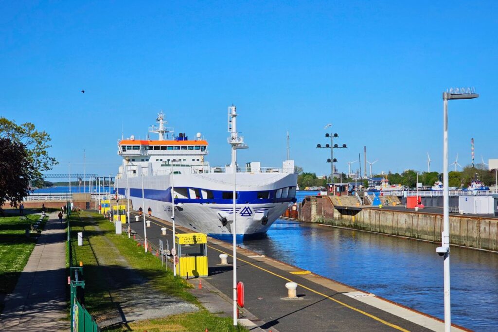 Ein großes weißes Frachtschiff passiert die Schleusenanlage in Brunsbüttel am Nord-Ostsee-Kanal bei sonnigem Wetter.