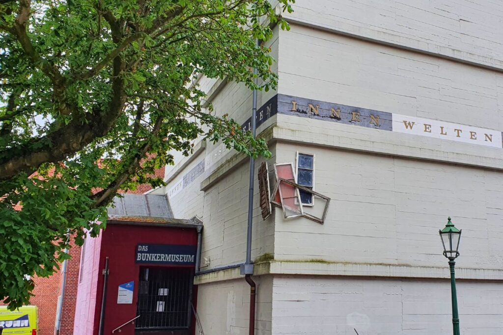 Die wuchtige graue Betonfassade des Bunkermuseums Emden mit der Aufschrift „INNEN WELTEN“ und einem Kunstfenster über dem Eingang.