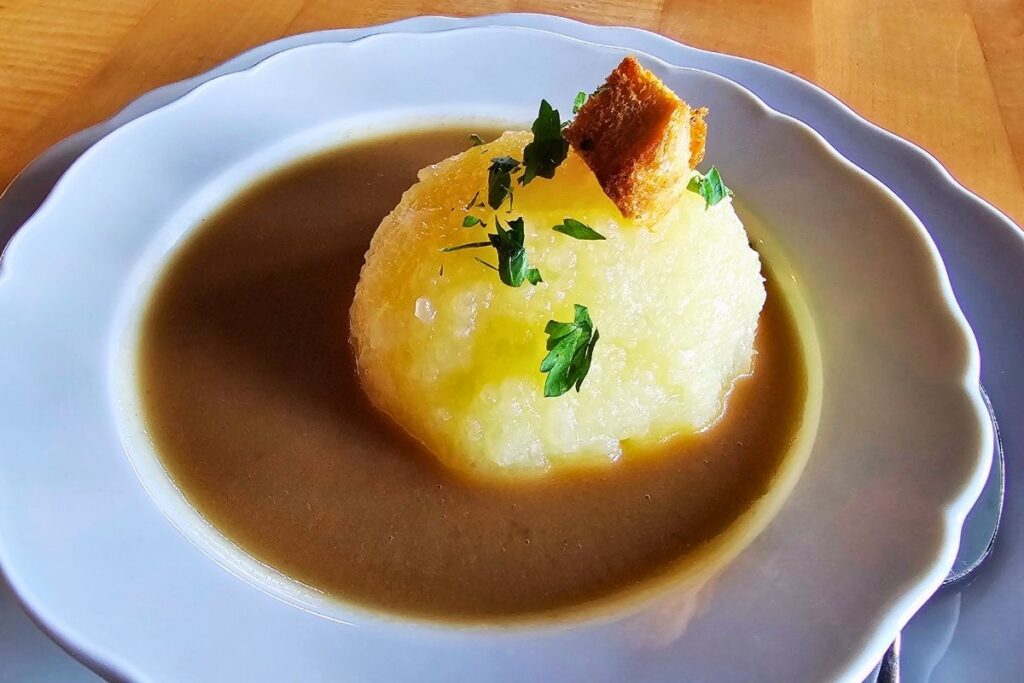 Ein weicher Coburger Rutscher-Kartoffelkloß mit gerösteten Brotwürfeln und Petersilie in dunkler Bratensoße auf einem weißen Porzellanteller in der Burgschänke der Veste Coburg.