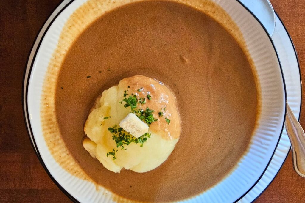 Ein einzelner, weicher Coburger Rutscher in reichlich dunkler Bratensauce mit Crouton und Petersilie in einem tiefen Teller im Ratskeller Coburg.
