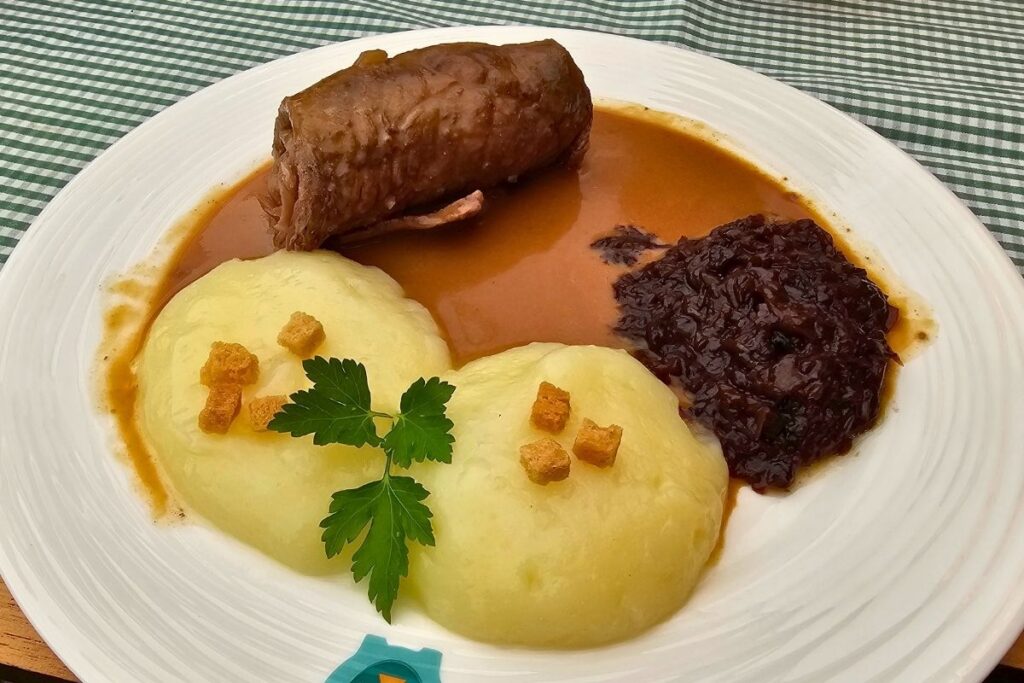 Ein weißer Teller mit einer saftigen Rinderroulade, dunkler Sauce, Apfelrotkohl und zwei Coburger Rutschern mit gerösteten Brotwürfeln im Restaurant Goldenes Kreuz.
