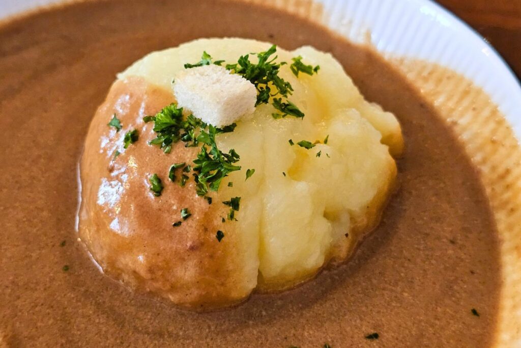 Nahaufnahme eines Coburger Rutschers in dunkler Bratensauce, bestreut mit frischer Petersilie und einem weißen Brotwürfel.