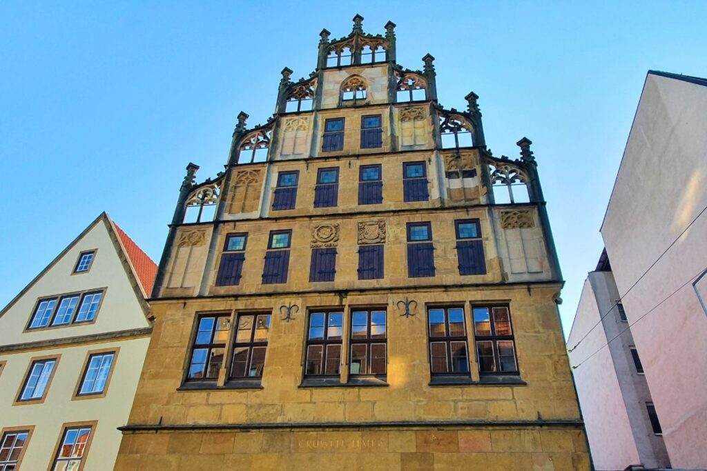 Der prachtvolle spätgotische Stufengiebel des historischen Crüwell-Hauses aus Sandstein mit filigranem Maßwerk unter blauem Himmel in Bielefeld.