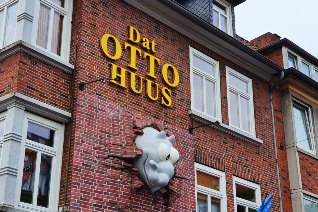 Rote Klinkerfassade des Otto-Huus in Emden mit einem dreidimensionalen grauen Ottifanten, der scheinbar durch die Ziegelmauer bricht.