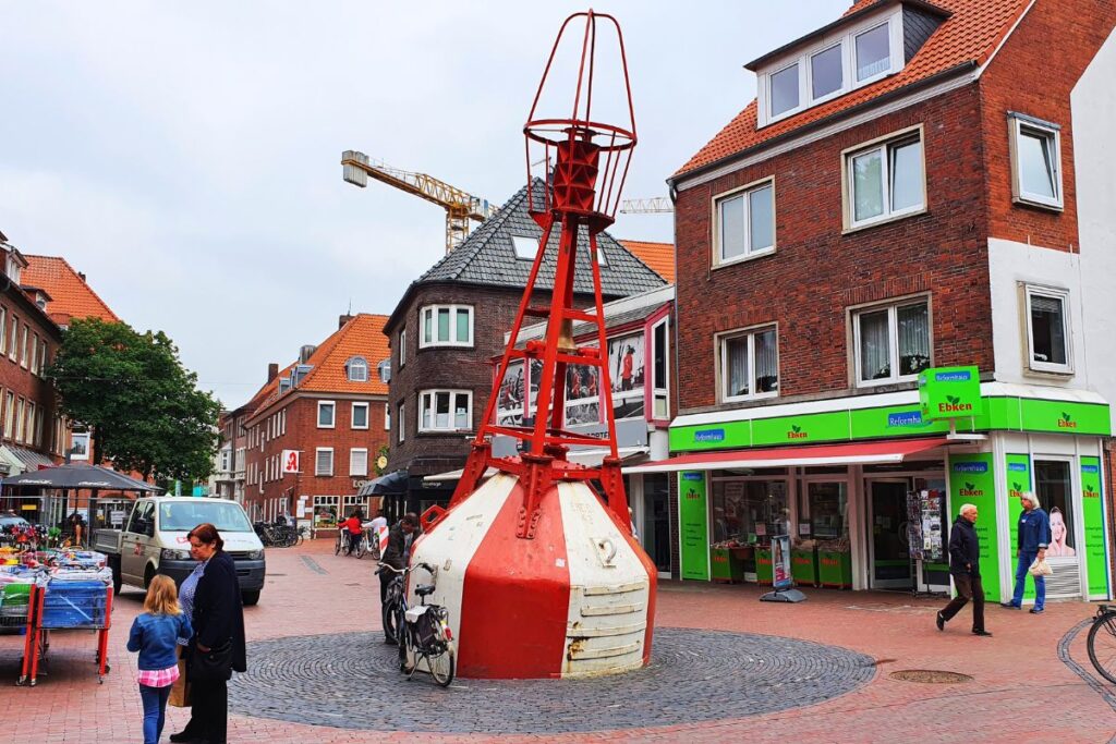 Eine rot-weiße Seetonne als maritimes Denkmal mitten auf einem gepflasterten Platz in der Fußgängerzone der Emder Innenstadt.