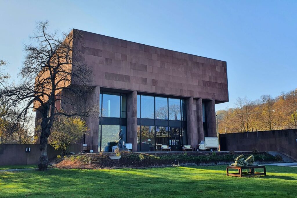 Der monumentale rote Sandsteinbau der Kunsthalle Bielefeld von Stararchitekt Philip Johnson mit Skulpturenpark auf einer grünen Wiese.