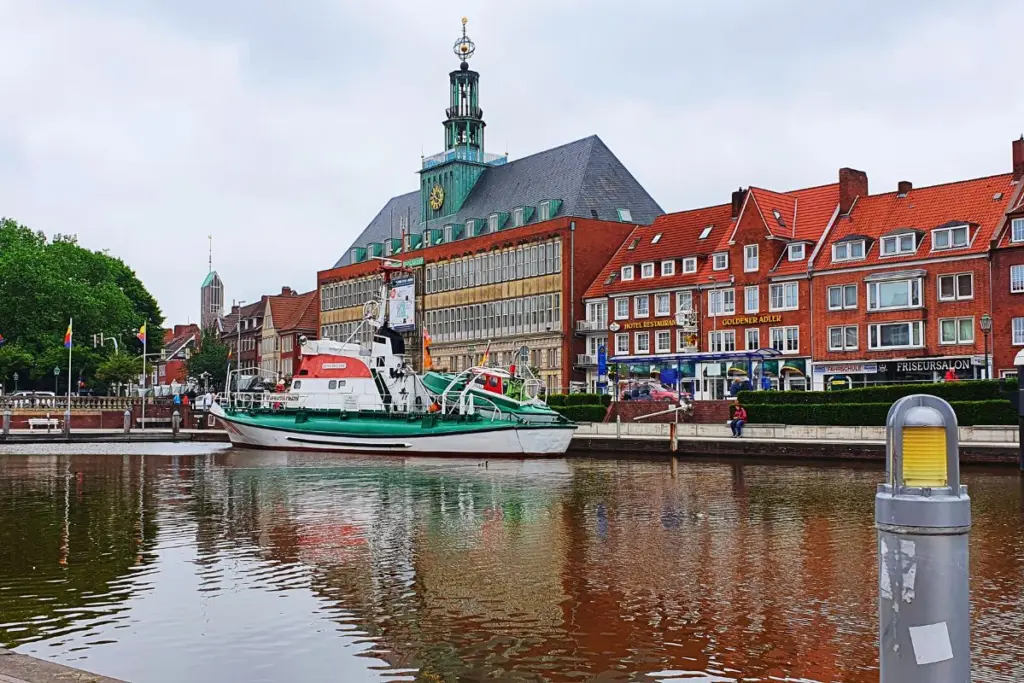 Der Ratsdelft in Emden mit dem historischen grün-weißen Seenotrettungskreuzer Georg Breusing auf spiegelndem Wasser vor der Kulisse des Rathausturms.