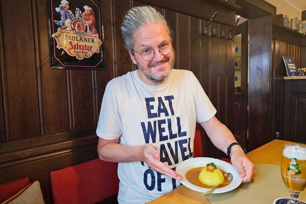 Reiseblogger Nicolo Martin lächelt am Holztisch und präsentiert einen dampfenden Teller Coburger Rutscher in dunkler Soße im traditionsreichen Restaurant Loreley.